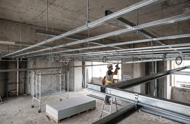 Pekerja konstruksi memasang bingkai plafon gipsum logam di situs interior