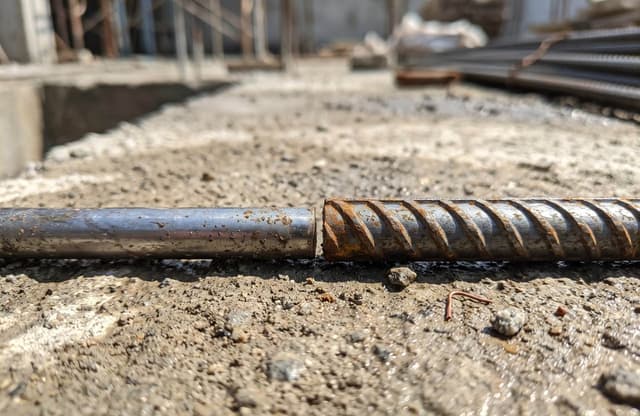 Perbedaan fisik permukaan besi beton 8mm polos dan besi beton 10mm ulir di lokasi proyek konstruksi.